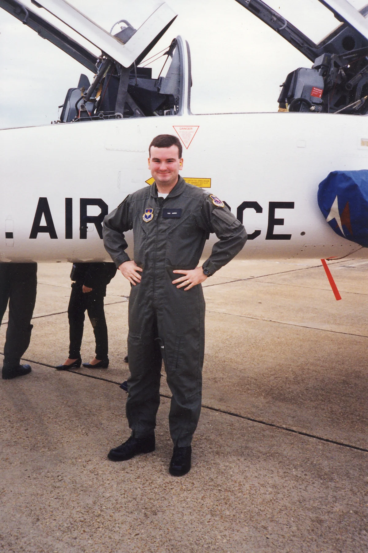 Tori L. Harris in a U.S. Air Force flight suit, standing in front of a jet trainer aircraft with its canopy open